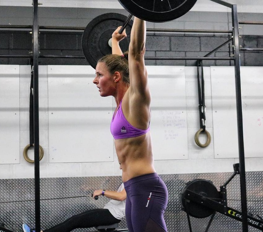 Stacie Tovar doing a heavy overhead press looking strong and ripped